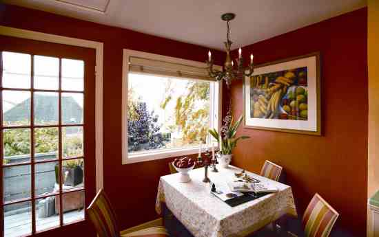 The deep color of the dining area’s walls suggests a sense of separation from the kitchen, offering vibrant contrast to the green foliage and blue sky outside.